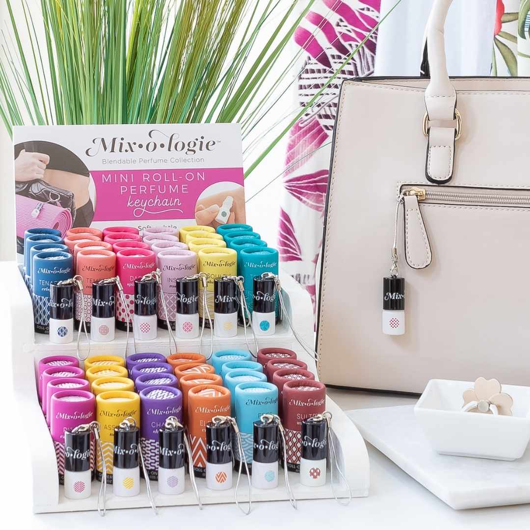 Retail display of Keychain Mini Roll-On Perfumes next to a purse and small white dish with green plant in background.