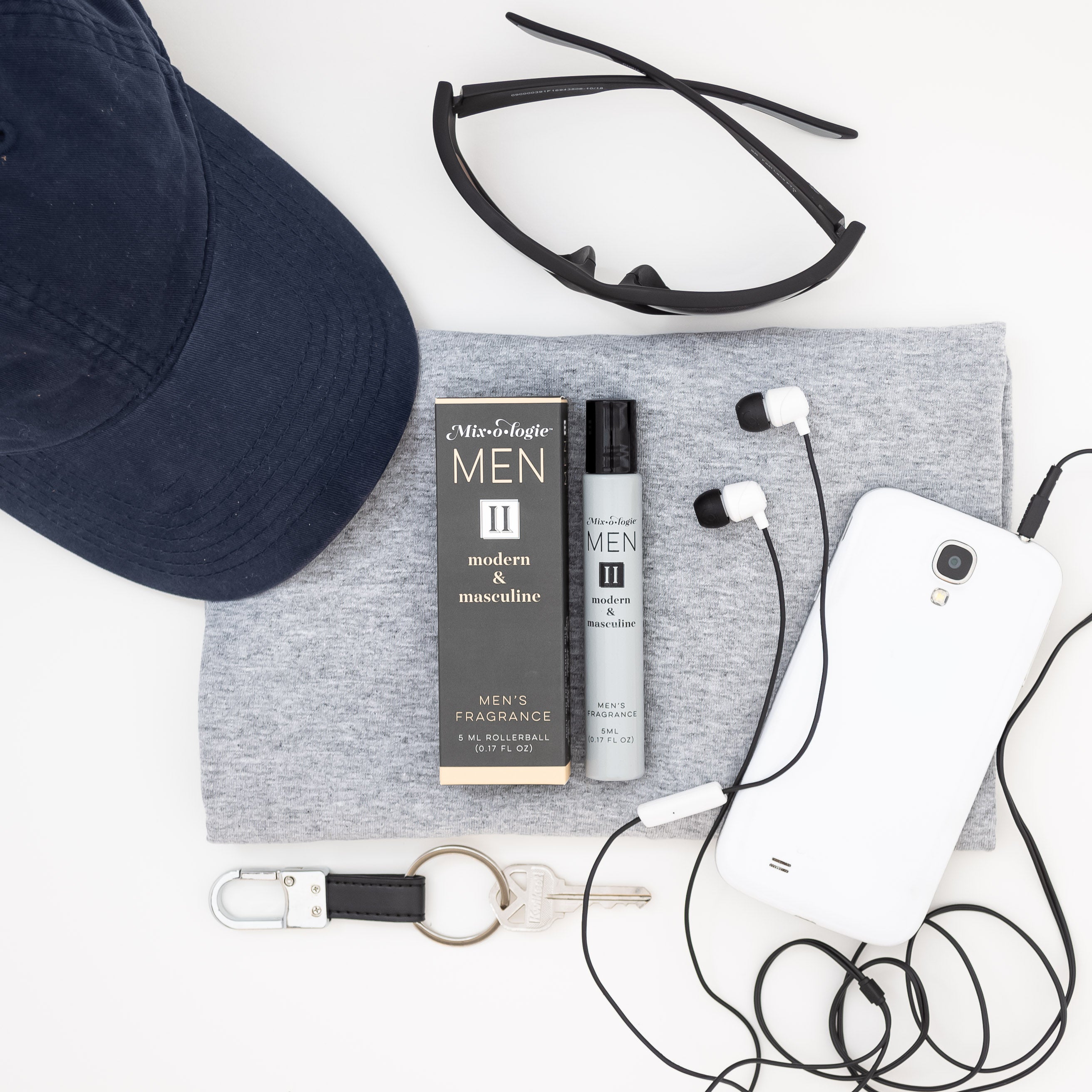 Mixologie rollerball scented with Men's II (Modern & Masculine) fragrance in 5 mL glass bottle displayed with hat, sunglasses, ipod and headphones..