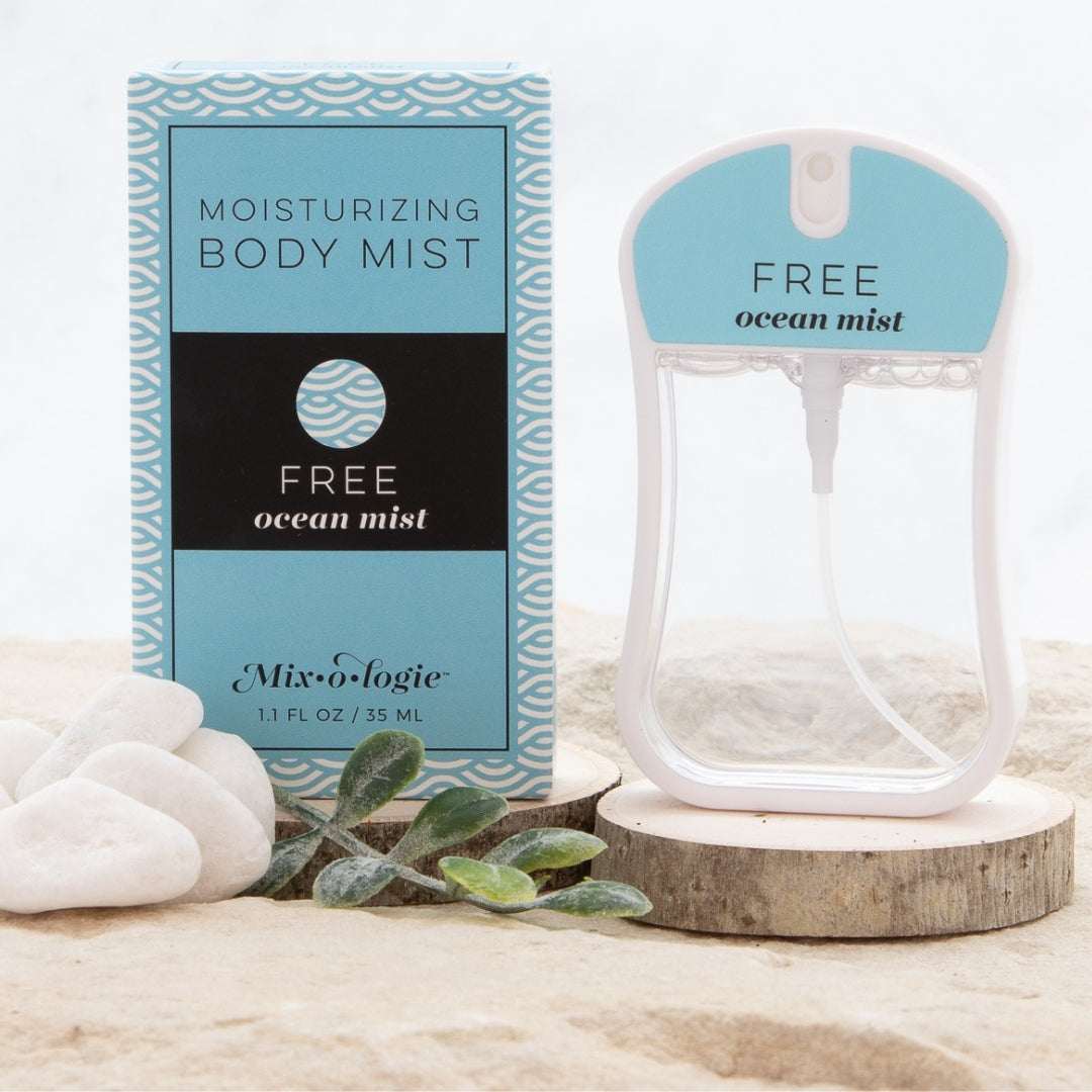 Moisturizing body mist scented with Mixologie's Free (ocean mist) scent in 35 mL plastic spray bottle. displayed with packaging on sand