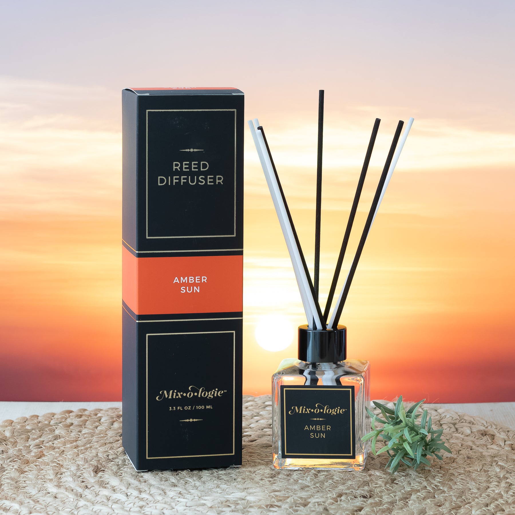 Mixologie Amber Sun scented Reed Diffuser 3.3 FL oz clear glass bottle with 8 diffuser reed sticks. Displayed in front of sunset. 