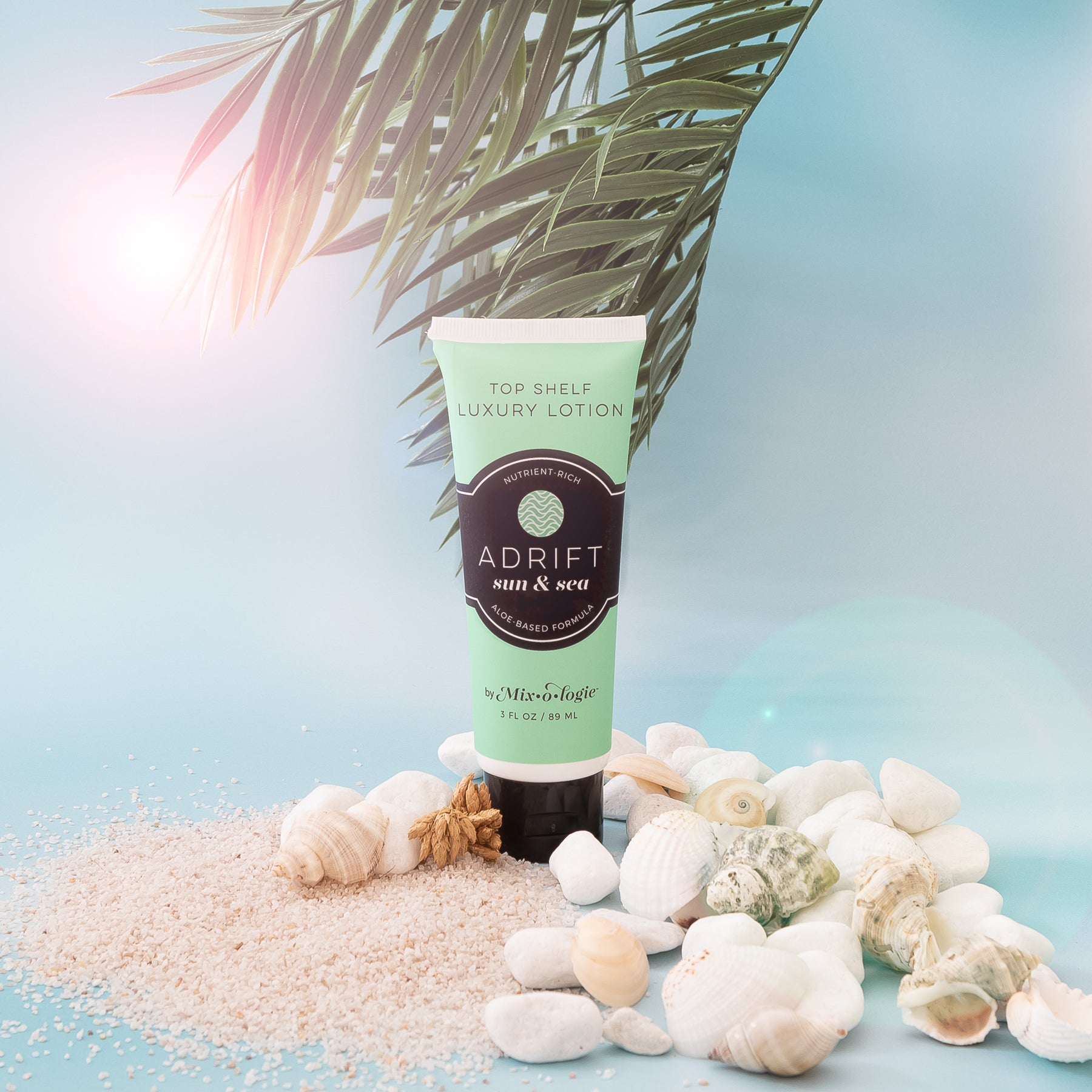 Adrift sun & sea aloe based lotion in 3 FL oz tube. Displayed on sand with shells and greenery. 